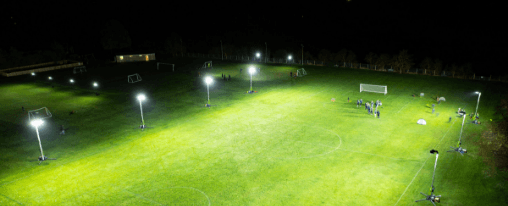 Flutlichtanlage auf einem beleuchteten Fu&szlig;ballplatz bei Nacht mit klar sichtbaren Flutlichtmasten und Spielfeld