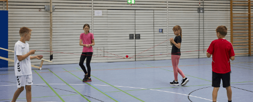 Teamspiele online kaufen im Kübler Sport Onlineshop Gruppe von Menschen beim gemeinsamen Spielen von Teamspielen im Freien, geeignet für Freizeit, Spaß und Zusammenhalt