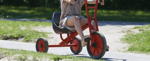 Mehrere Kinder fahren Dreirad im Freien auf einem Spielplatz