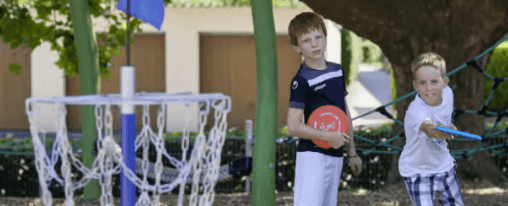 Personen spielen Disc Golf auf einer Freizeitanlage mit Fangkörben und Bahnen im Grünen