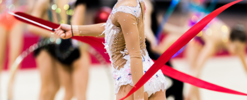 Tanzbänder online kaufen im Kübler Sport Onlineshop Gymnastin trainiert mit farbenfrohem Rhythmikband in heller Sporthalle