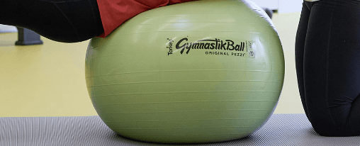 Pezziball als Gymnastikball in einer therapeutischen Anwendung von Erwachsenen und Kindern in einer Praxisumgebung