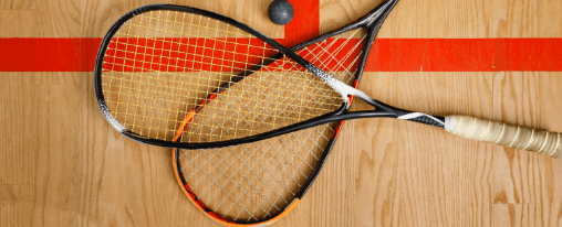 Zwei Squashschl&auml;ger  neben einem Squashball auf einem Hallenboden