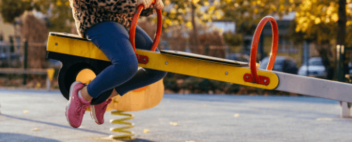Balkenwippe online kaufen im Kübler Sport Onlineshop Montierte Balkenwippe aus Metall auf einem modernen Kinderspielplatz mit mehreren Kindern beim Wippen