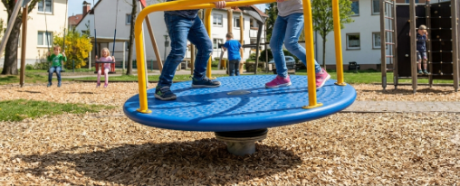 Kinder spielen auf einer Kreiselwippe als robustem Spielplatzger&auml;t im Freien