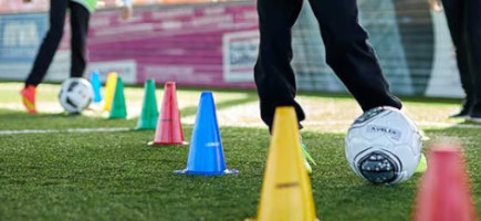 Fußballer dribbeln mit Fußbällen beim Training um Markierhütchen auf Sportplatz