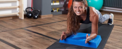 Athletin führt eine Plankübung auf einem Balance Pad und Fitnessmatte in einem Fitnessraum aus