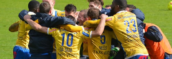 Fußballteam mit gelben Trikots Arm in Arm auf einem Fußballplatz