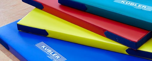 Anordnung einer dunkelblauen, gelben, roten und hellblauer Kübler Sport Matte übereinander