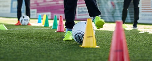 Fußballspieler trainieren Dribbles um Markierhütchen auf Sportplatz