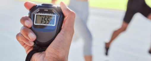 Leichtathletik Zeitmessgeräte bei Kübler Sport kaufen Mensch hält ein Zeitmessgerät während im Hintergrund Leute joggen