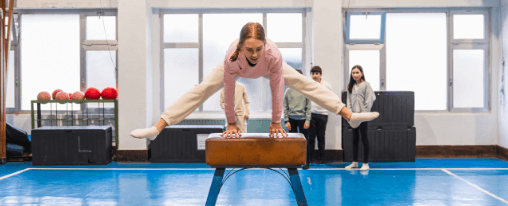 Sprungpferd für Turnunterricht bei Kübler Sport kaufen Frontalaufnahme einer Schülerin, die über ein Sprungpferd in der Turnhalle springt