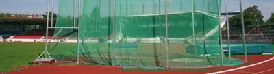 Abwurfanlage auf einem Sportplatz mit grünem Netz und roter Tartanbahn