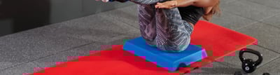 Frau trainiert auf einem Balance Pad und einer Fitnessmatte
