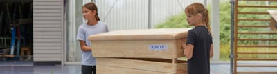 Zwei Kinder in der Sporthalle heben den Deckel eines Kübler Sport Sprungkastens an