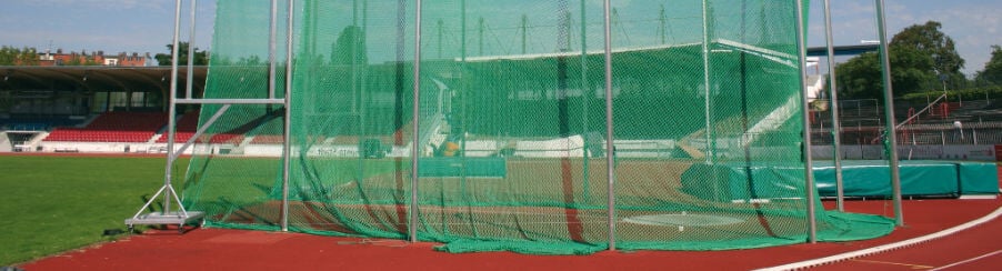 Abwurfanlage auf einem Sportplatz mit grünem Netz und roter Tartanbahn