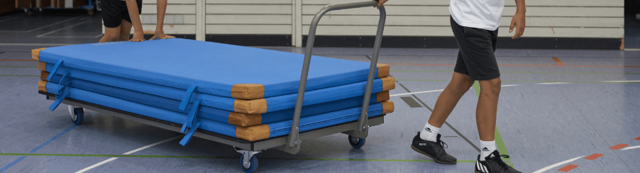 Vier Turnmatten von Kübler Sport in Blau mit braunen Lederecken auf einem Mattenwagen