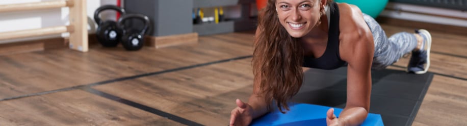 Frau in einem Fitnessraum macht auf einer Fitnessmatte mit einem Balance Pad eine Plank