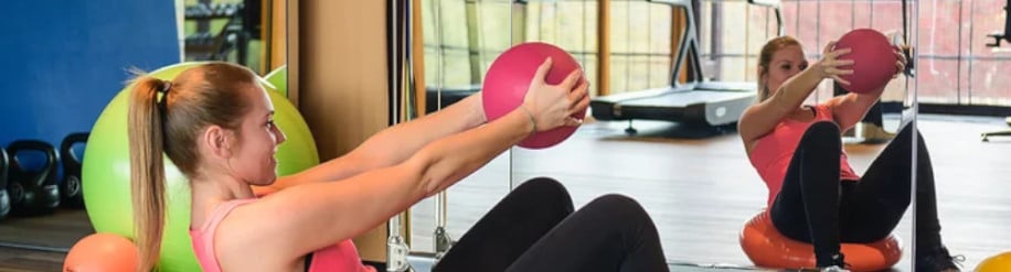 Frau macht im Fitness Übungen mit einem pinken Medizinball