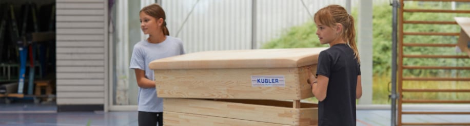 Zwei Kinder in der Sporthalle heben den Deckel eines Kübler Sport Sprungkastens an