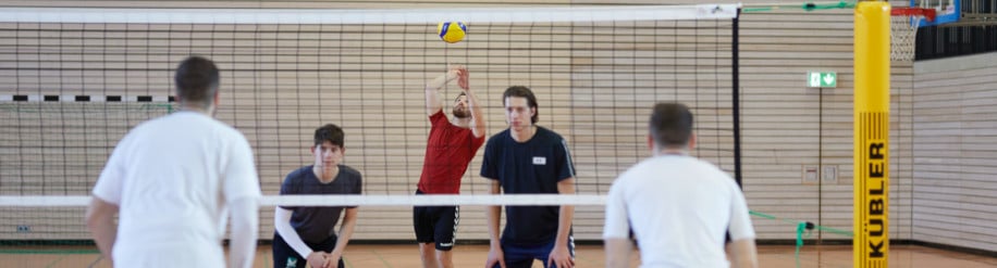 Ein Gruppe Männer spielt in der Turnhalle Volleyball mit einem Kübler Sport Volleyballnetz