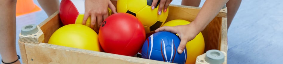 Mehrere Softbälle in einem kleinen umgedrehten Turnkasten in einer Sporthalle