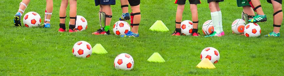 Mehrere Spieler mit vielen Fußbällen und Markierhütchen auf einem Rasenplatz