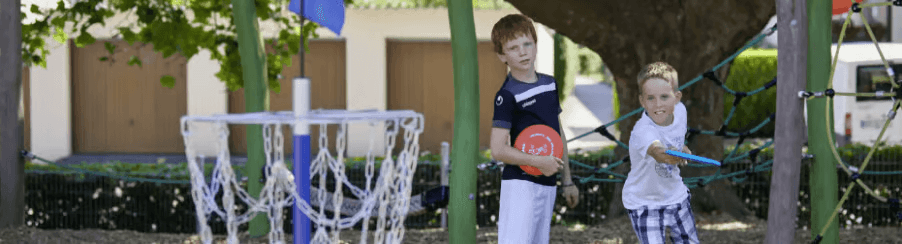Personen spielen Disc Golf auf einer Freizeitanlage mit Fangkörben und Bahnen im Grünen