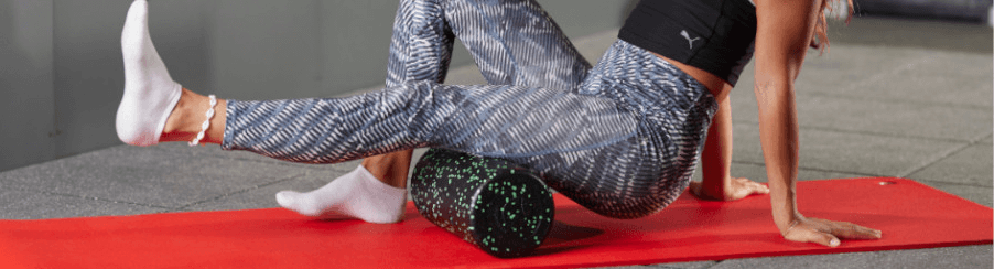 Frau macht auf einer roten Fitnessmatte Übungen mit einer schwarzen Faszienrolle