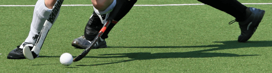 Teamsportler spielen Feldhockey auf dem Spielfeld mit passender Ausrüstung aus dem Feldhockeyshop