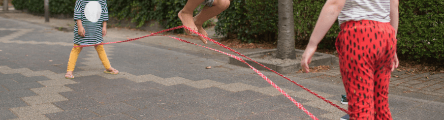 Kinder und Erwachsene spielen mit buntem Gummitwist als Bewegungsspiel im Freien – ideal für Freizeit, Schule und Pausen