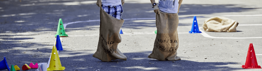 Kinder und Erwachsene beim Sackhüpfen mit bunten Hüpfsäcken auf einer Wiese bei einem Freizeitspiel