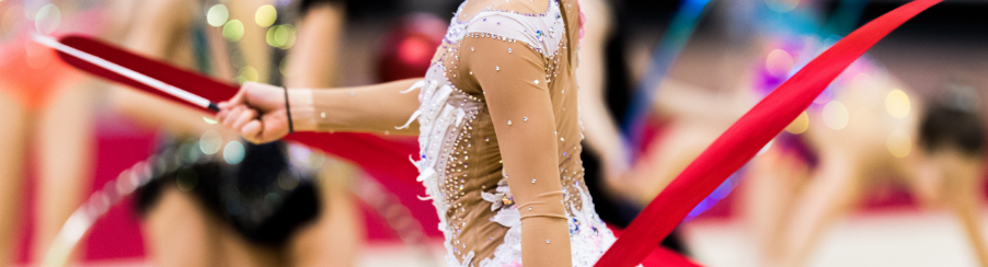 Gymnastin trainiert mit farbenfrohem Rhythmikband in heller Sporthalle
