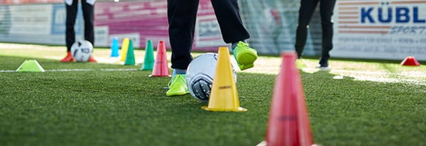 Fußballspieler trainieren Dribbles um Markierhütchen auf Sportplatz