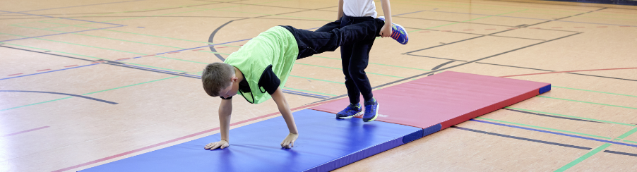 Kinder auf zwei bunten Fallschutzmatten üben Schubkarren-Laufen