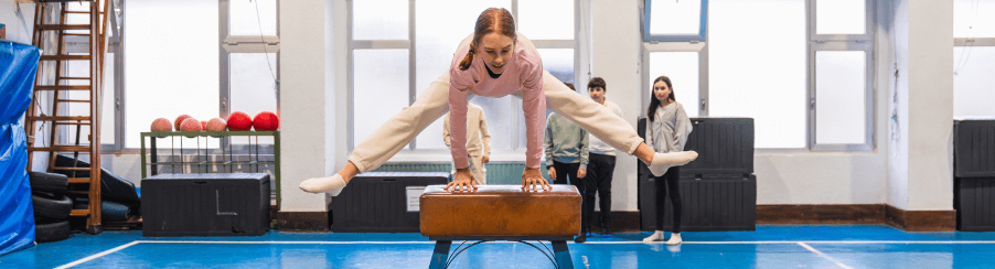 Schülerin springt über ein Sprungpferd in einer Turnhalle